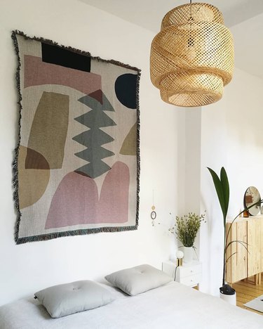 Boho apartment decor in bedroom with geometric tapestry and bamboo pendant light