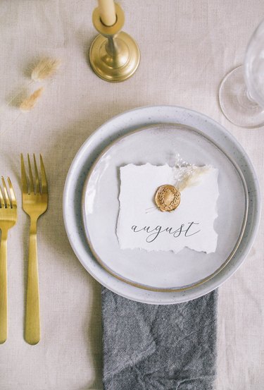 DIY gold wax seal place card with dried florals on top of place setting on table