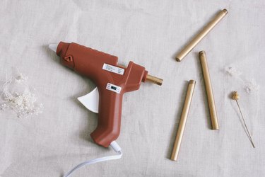 Three gold sealing wax sticks next to glue gun loaded with wax stick