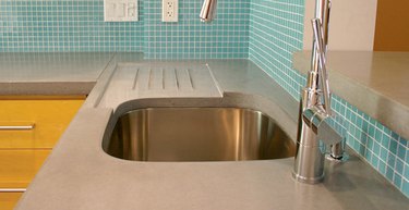 Concrete kitchen countertop with embedded drainboard and teal tile backsplash