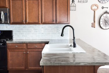 Feather-finish concrete kitchen countertops in with wood cabinets and white-washed brick backsplash