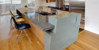 Tricolored concrete island in modern kitchen with wood floors and Eames chairs