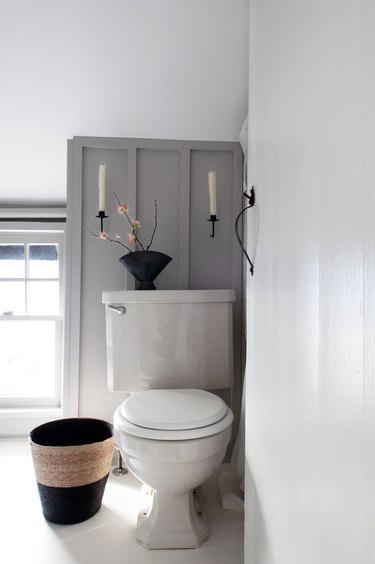 white toilet next to wastebasket in bathroom with grey walls and sconces