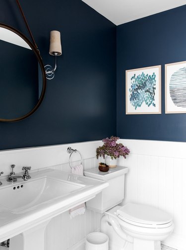 navy powder room with paintings and wood paneling