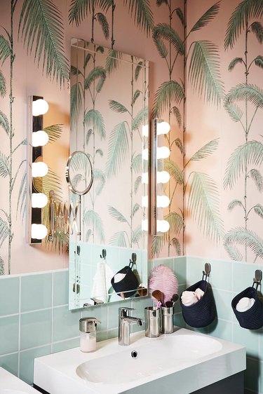 IKEA bathroom lighting idea with wall sconces next to mirror and palm leaf wallpaper