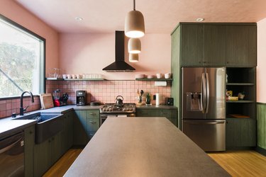 view of kitchen island with dark countertop, green kitchen cabinets, stainless steel appliances and pink walls and backsplash
