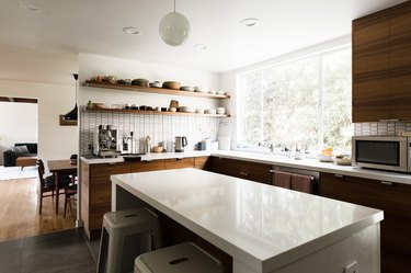 kitchen island with white stone countertop; dark wood kitchen cabinets; open concept to dining room