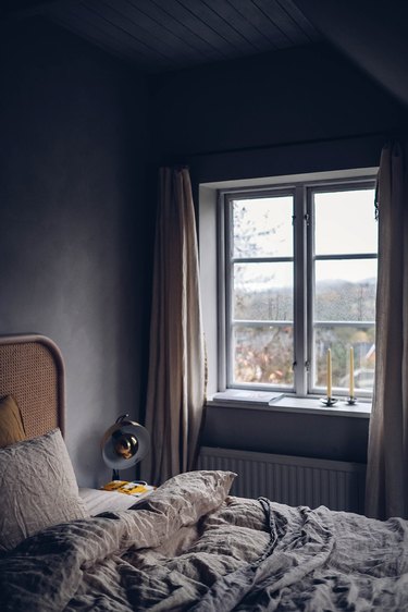 rattan bed in dark minimalist bedroom with linen duvet cover