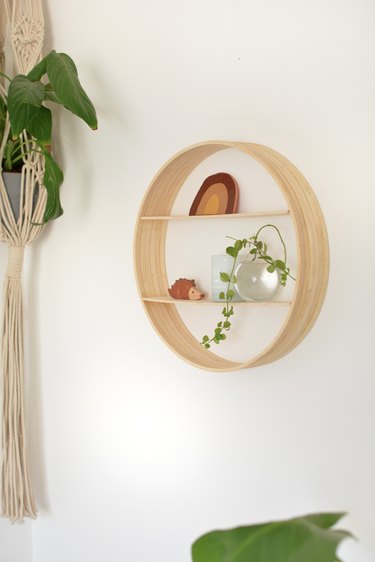 Wooden circle with small trinkets on shelves hanging on wall.