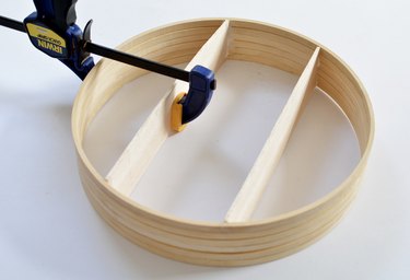 Wooden circular shelf with hand clamp holding shelf while glue dries.