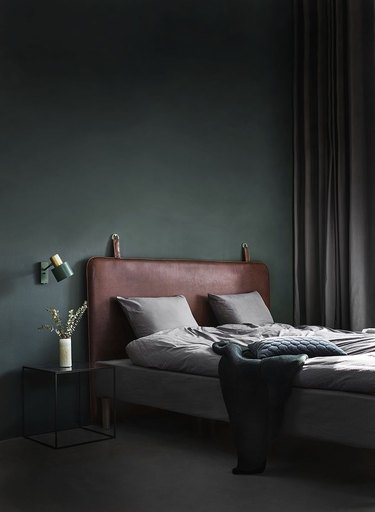 leather headboard in dark minimalist bedroom with turquoise wall sconce