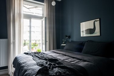dark minimalist bedroom with deep blue wall paint and white curtains