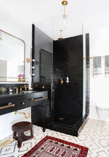 bright-white bathroom with shiny glazed black tile shower, brass fixtures, and vintage rug