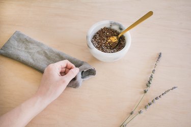 Spooning scented flax seed and lavender buds into opening of eye pillow