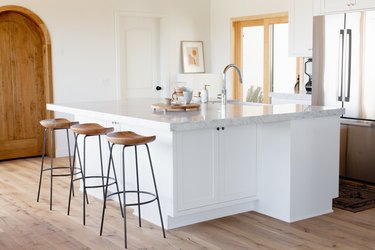 white kitchen island with light stone countertop, barstools and sink