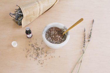 Mixing flax seeds, dried lavender and essential oil in marble bowl