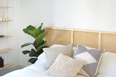 DIY cane headboard on bed with bohemian pillows and plant next to the bed.