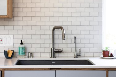 kitchen sink and faucet with white subway tile backsplash and garbage disposal buttons