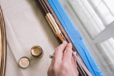 Painting gilding paint onto wooden mirror frame with small paintbrush