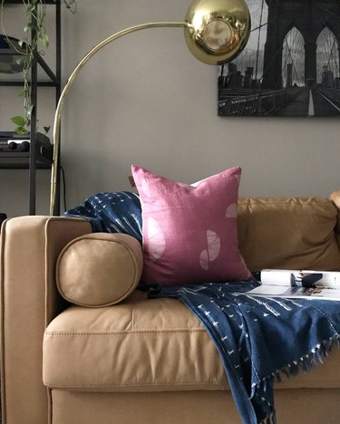 beige couch with gold floor lamp, pink pillow, and blue blanket