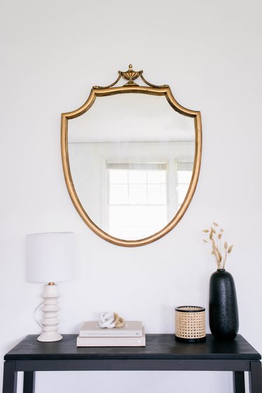 DIY gold gilt mirror hanging on wall above black table with lamp, books and vase