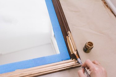 Painting gilding paint onto wooden mirror frame with small paintbrush