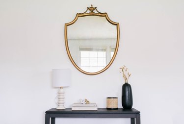 DIY gilded mirror hanging on wall above black table with lamp, books, and vases