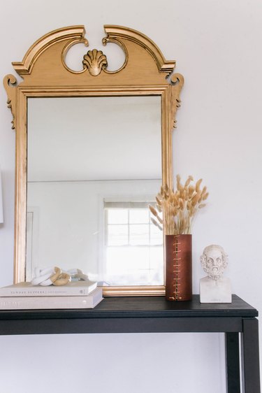 DIY antique gilt mirror leaned against wall on black table with books, vase and bust