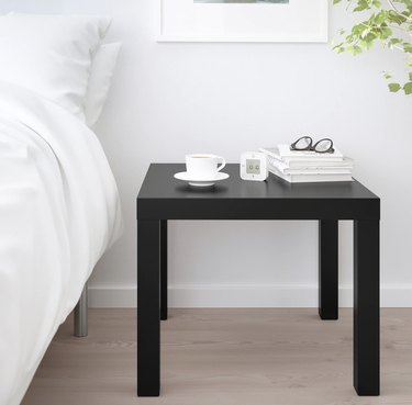 IKEA's LACK side table in black next to a bed with white bedding