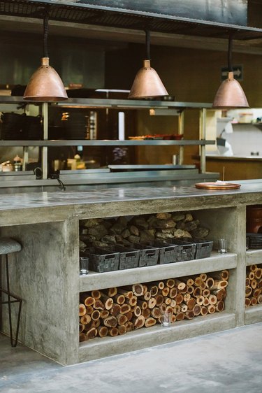 Large outdoor industrial kitchen with copper pendant lighting and wood log storage