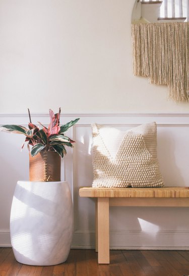 DIY leather wrapped planter with pink and green leaf plant on marble stool next to bench