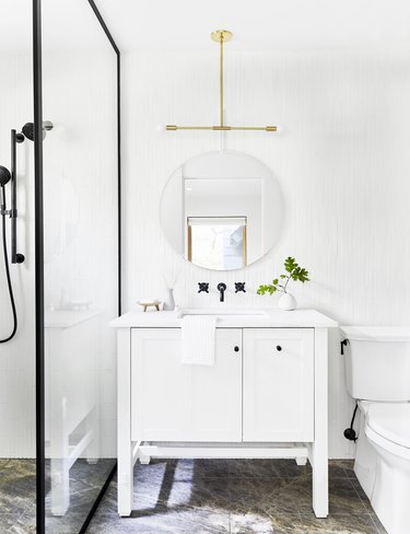 White modern Scandinavian bathroom vanity with white vanity, black steel-paned shower, and brass pendant light