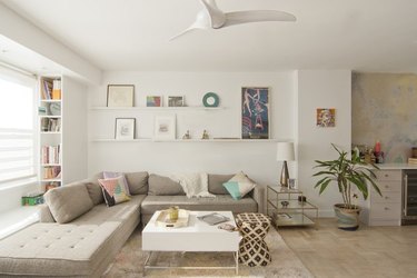 neutral living room with floating shelves and ceiling fan