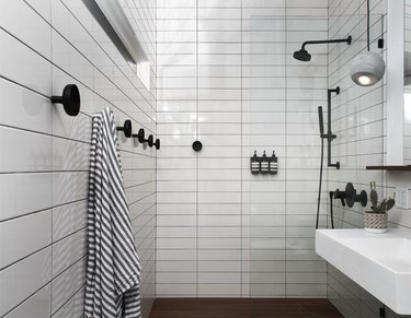 white subway shower tile ideas in bathroom with matte black fixtures and striped towel