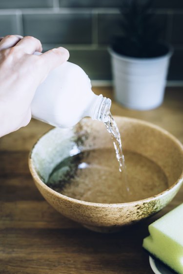 person pouring clear liquid into light brown porcelain bowl