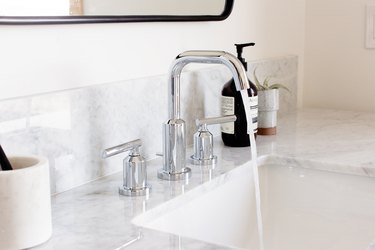 white marble sink with silver fixtures featuring water running and Aesop hand soap