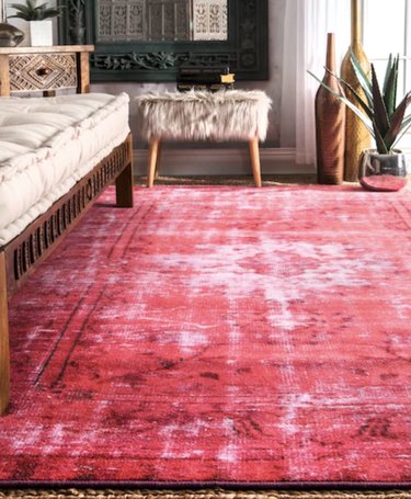 living room rug idea with a bright pink rug under a wood-framed couch, with a faux-fur ottoman in the background