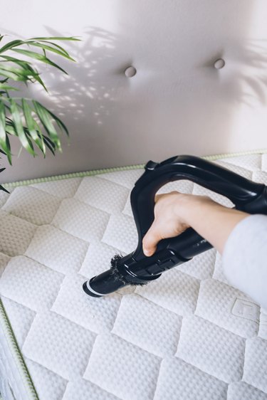 person using black vacuum handle to clean white quilted mattress