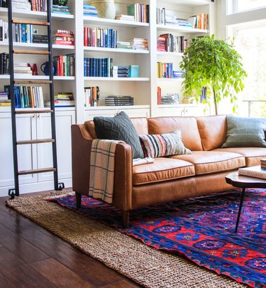 living room rug idea with leather couch in a home library, placed on a bright blue and red vintage rug, layered over a jute area rug