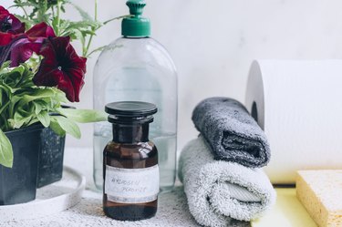 small brown bottle labelled hydrogen peroxide sitting next to two small towels, paper towel, soap bottle, and plant