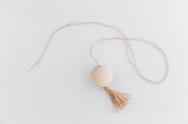 Thread the long twine end through the wood ball and pull it through until the tassel hits the bottom of the ball.