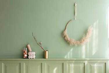 DIY minimalist wreath with pampas grass on brass ring hanging on green wall above matching buffet