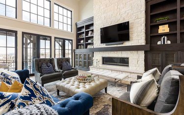 transitional family room with two leather high back chairs, leather tufted ottoman, blue tufted couch, stone mantel