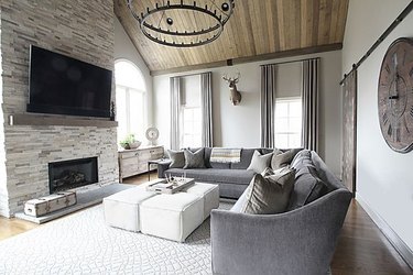transitional family room with gray sectional couch, white ottomans, wood ceiling, iron chandelier.