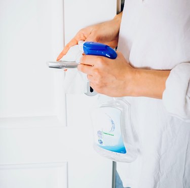 Woman cleaning door handle with cleaning spray