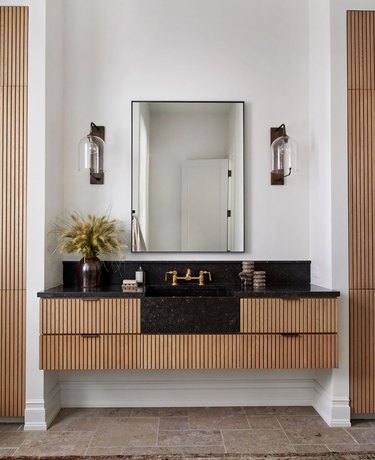elegant bathroom lighting idea with black counter, corrugated drawers