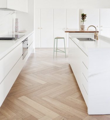 white kitchens with wood floors in herringbone pattern and brass faucet