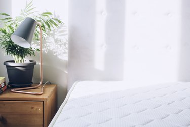 White mattress next to nightstand with lamp and plant