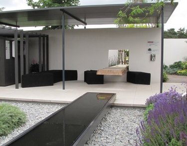 Covered modern pergola with metal roofing, black couch and chairs, modern fountain and native plants.