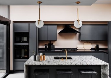 Kitchen with black cabinets and counters, terrazzo waterfall kitchen island, sink.